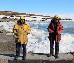 Two men stand by in large jackets watching the swimmers as part of the safety crew