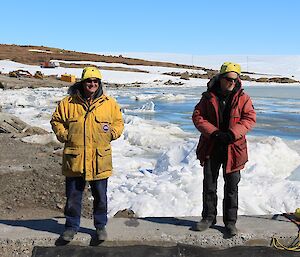 Two men stand by in large jackets watching the swimmers as part of the safety crew