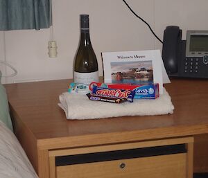 Chocolates, toothpaste, wine and a freshly folded towel on a bedside table