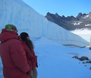 Two expeditioners in red goose down jackets looking up a steep rock face