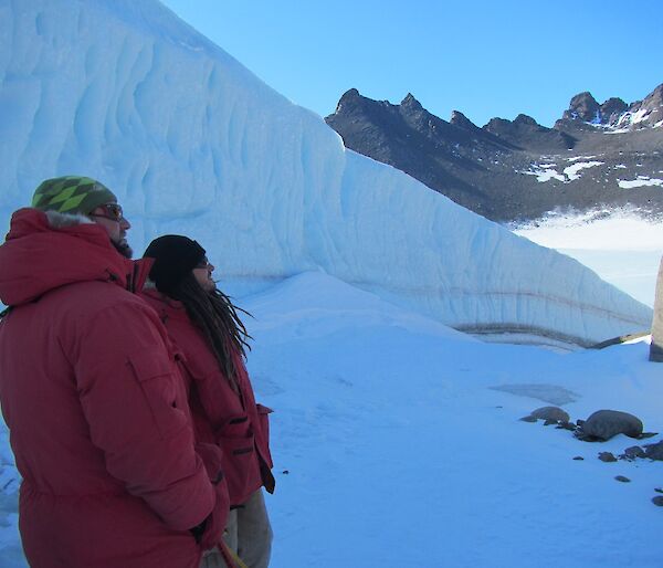 Two expeditioners in red goose down jackets looking up a steep rock face