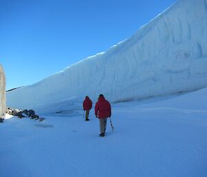 two men walking along the base of an ice cliff
