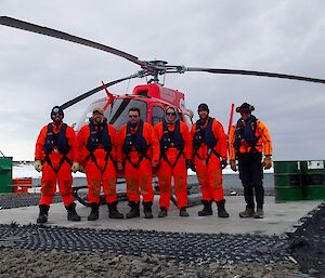 Six men dressed in orange immersion suits and lifejackets in front of a B3 helicopter