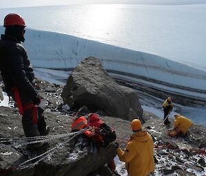 Six team members lowering a stretcher down a steep hill using ropes