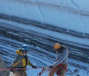 Two men abseiling down a rock face with a stretcher