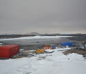a horse shoe shaped harbour with large red building and smaller bright coloured buildings on shore. The surface of the water has a layer of ice that looks like grease