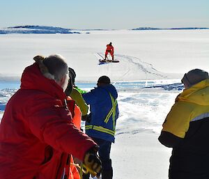 Six men pulling a ice platform in via a rope