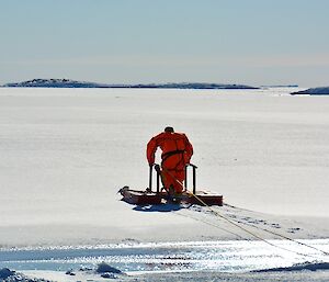 A man in an dry suit with a floating platform walking over the sea ice