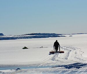 One man walking on the ice using a rescue platform to retrieve a person on the ice