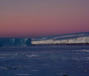 A pink and blue sunset over a glacier and ice berg
