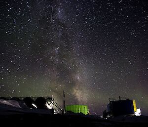 the night sky with the milky way above a green building and a slight green aurora