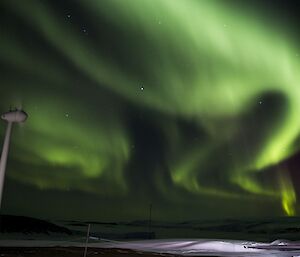 A large green aurora above a wind turbine