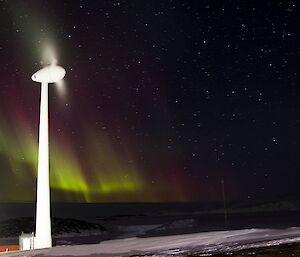 Slight pink and green aurora behind a wind turbine