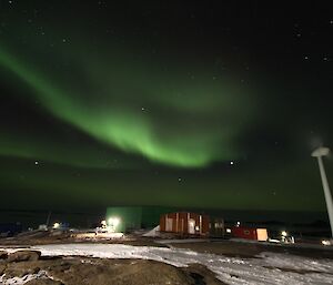 A large green aurora above an old rust coloured building