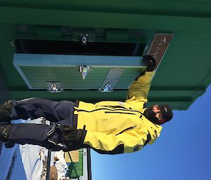 A man in yellow jacket standing outside a green hut