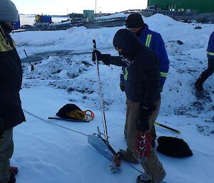 Three men stand around a hand winch in the snow