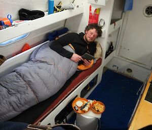 A man lying down in a sleeping bag eating a cheese platter