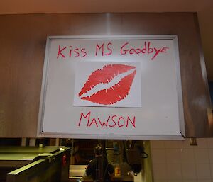 A white board with Kiss MS Goodbye in red writing and a large pair of lips