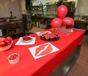 a table with apples, jaffas, red snakes and cupcakes all decorated with red balloons