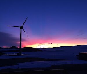 a sunrise with a wind turbine in front