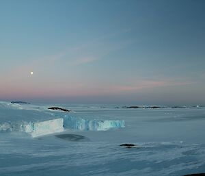 a glacier at sunrise with a full moon in the sky