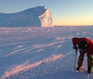 A man using a electric drill to drill a hole in the sea ice