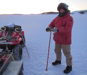 A man with a measuring stick that is in the ice