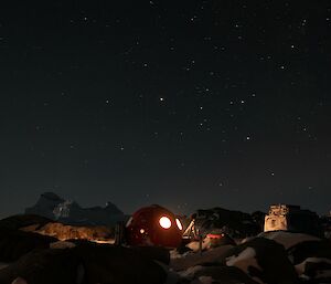 A red hut with lights shining in the windows and the stars out