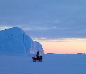 A quad bike and rider in front of a iceberg