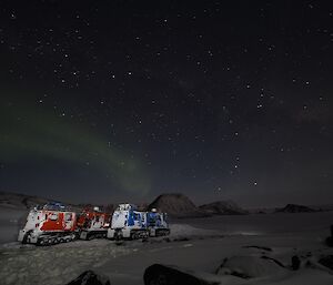 two hagglunds on the ice with an aurora overhead