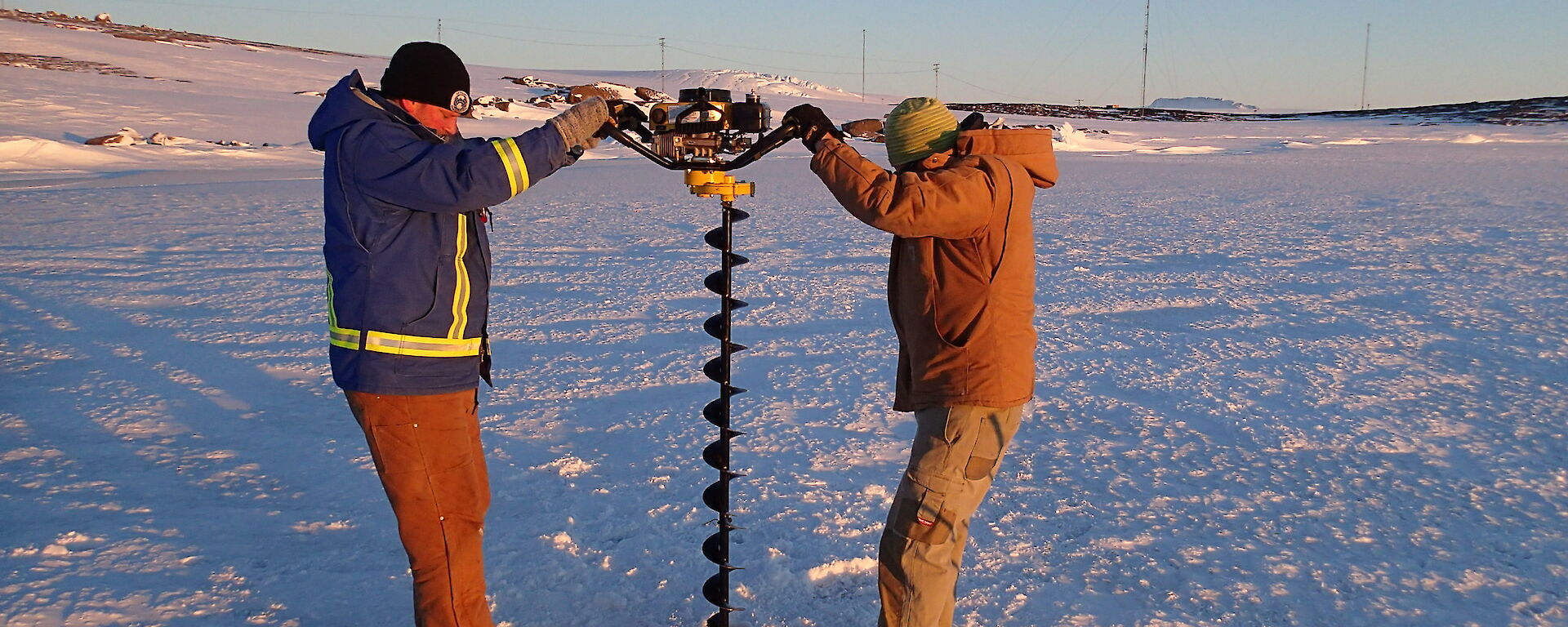 Two men with a large bore drill making a hole in the sea ice