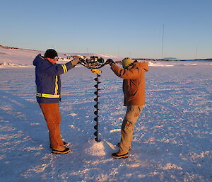 Two men with a large bore drill making a hole in the sea ice