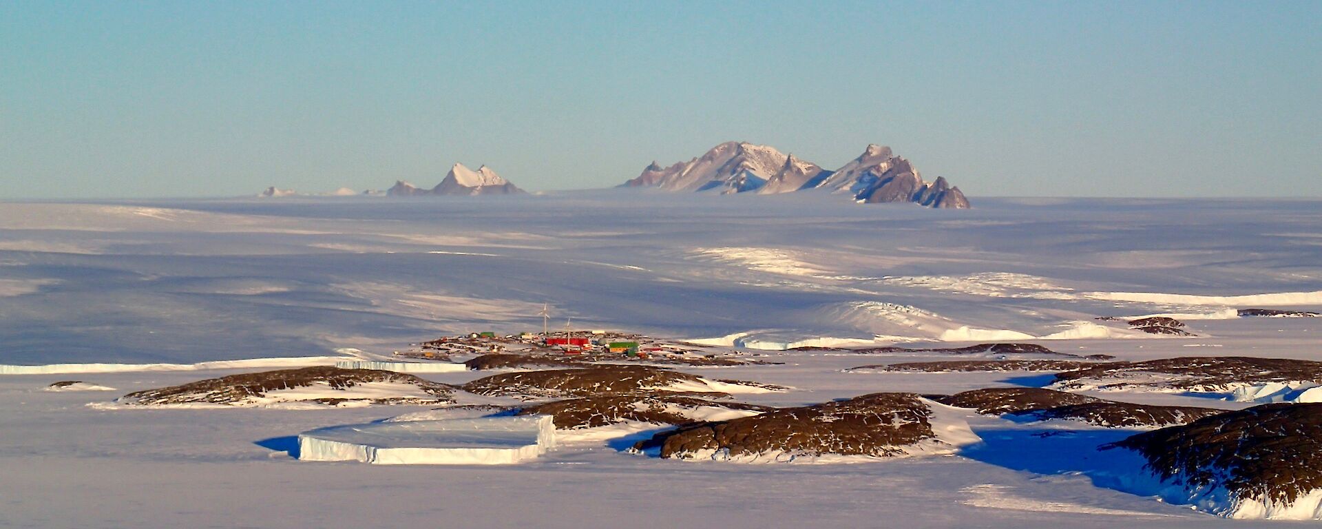 A small collection of buildings on the water edge with Mountain ranges in the background.