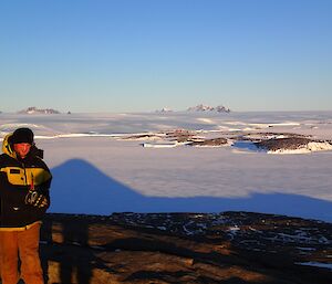 A man on a hilltop and Mawson station behind.