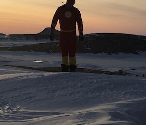 A man silouetted against the sunrise dressed as a super hero