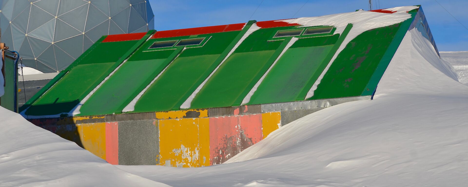 a hut made of multicoloured yellow and pink panels with a green roof