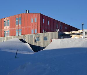 A old style hut dwarfed by a large red modern building