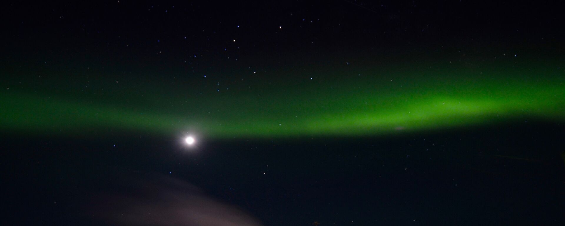 A green aurora across the sky with a moon in the middle