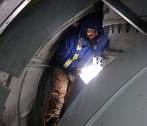 An electrician working in a small nose cone area of the wind turbine