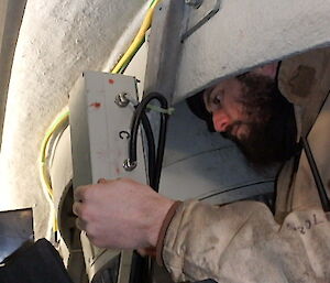 an electrician working inside a very small space replacing a bracket