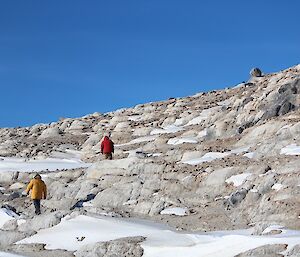 A rocky hillside with two people walking up it to where the snow petrel camera is located