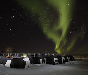 A green aurora behind a blizzard tail and a Mawson sign