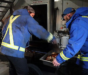 Two expeditioners getting the cooked pig off a spit ready to eat