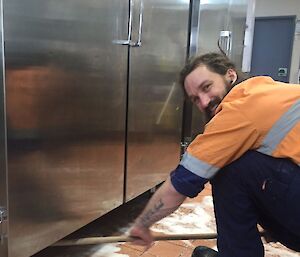 A man scrubbing underneath the large fridges