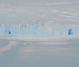 a large ice cliff with two ice caves against sea ice