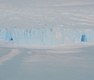 a large ice cliff with two ice caves against sea ice