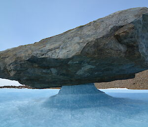 A large rock balanced on a pedestal of ice