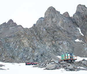 Seven quads on the snow beside Rumdoodle hut with the rocks of the North Masson Range behind