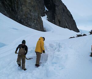 Two expeditioners digging in the snow to make a shelter