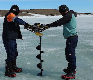 Tony Harris and Ben Newport on each side of the auger, holding it as they drill into the sea ice above the tide gauge casing